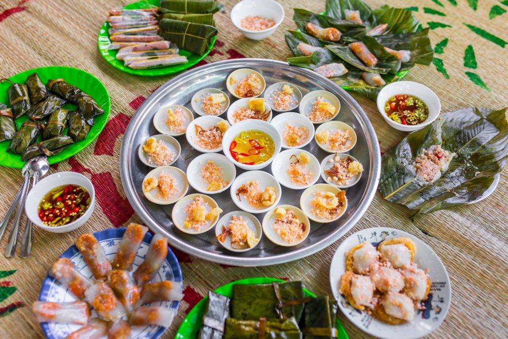 돗자리 위에 차린 후에 떡 요리 한 상. 작은 흰 종지에 담긴 반배오 쟁반, 바나나 잎에 싼 떡, 반투명한 타피오카 떡, 바삭한 받침의 떡, 그리고 느억맘과 고추 종지